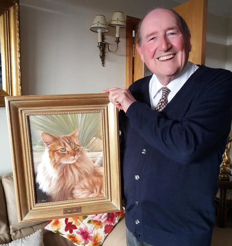 Happy client holding the framed oil portrait of Roly the cat.