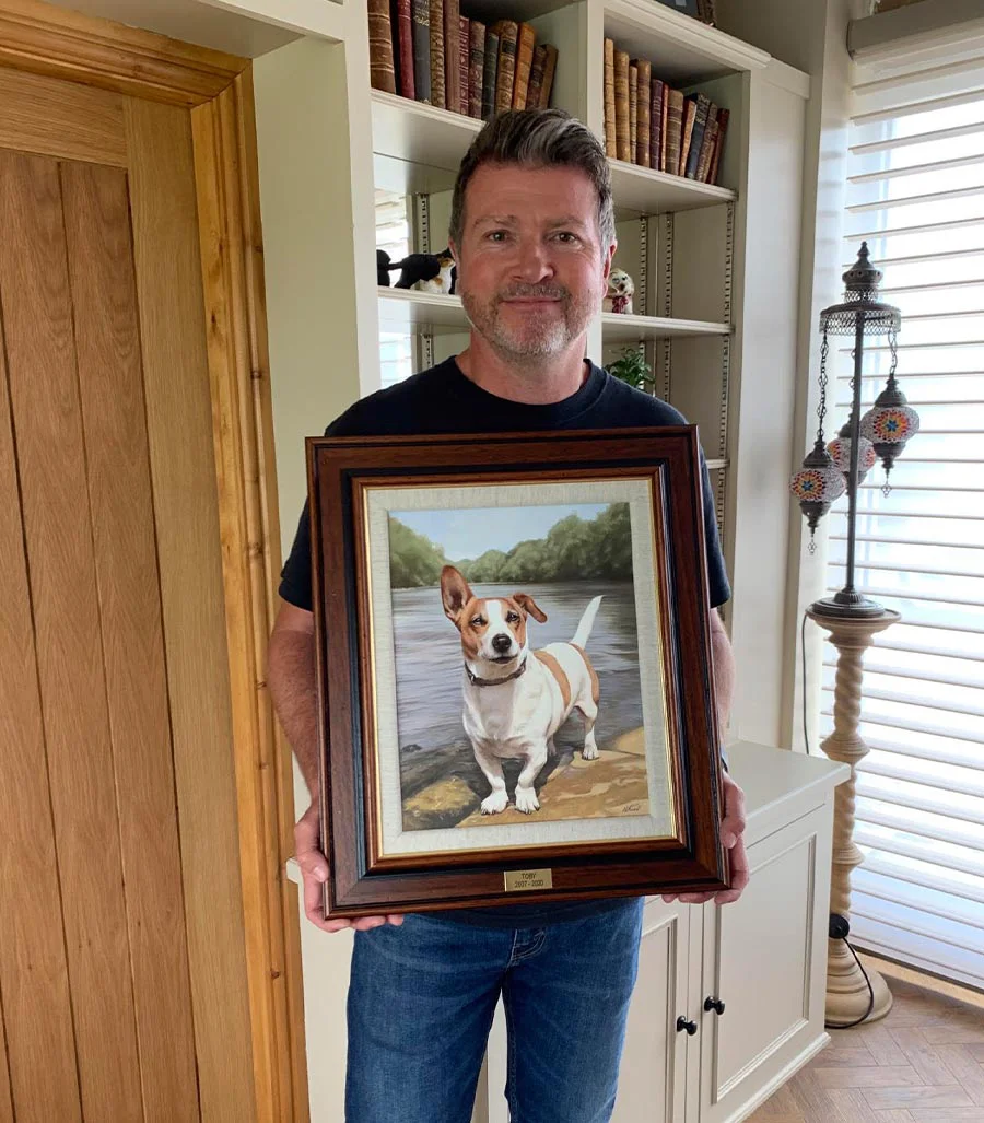 A unique gift: Hand-painted portrait of Toby the dog by Nicholas Beall A man smiling while holding a framed oil painting of his dog, Toby, by artist Nicholas Beall.