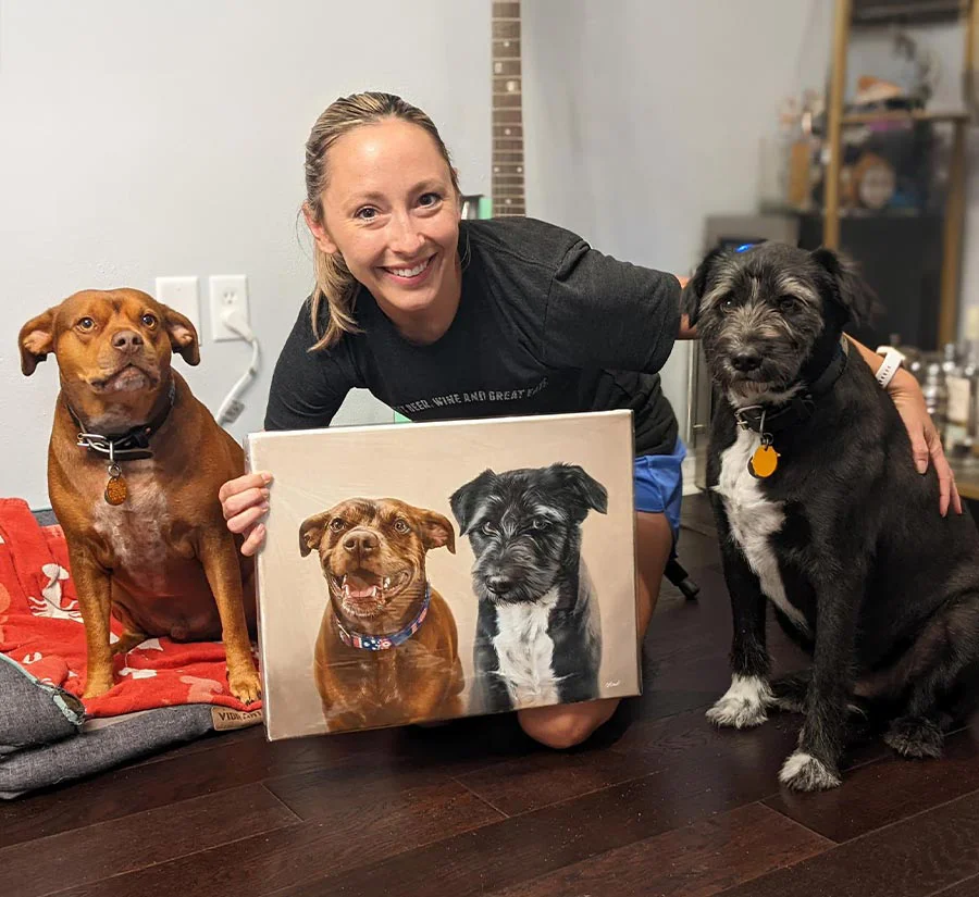 Surprise oil portrait gift of Shadow and Moose delivered to the USA by Nicholas Beall Jen smiling joyfully while holding a surprise oil portrait of her dogs, Shadow and Moose, delivered to the USA.