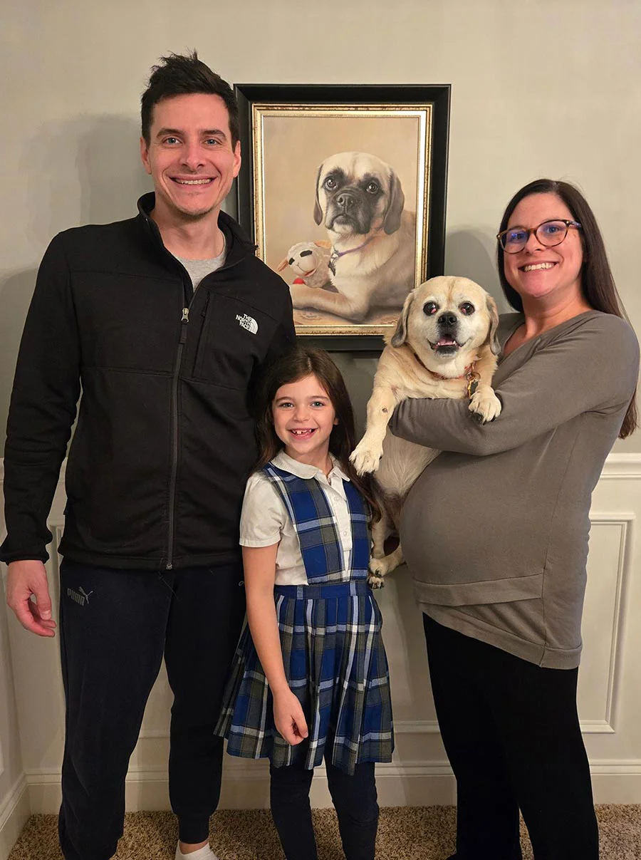 A family's cherished oil pet portrait with their dog, Sonny, and Gabby's portrait A smiling family posing with their dog, Sonny, and a beautiful framed oil portrait of another dog, Gabby, by Nicholas Beall, displayed in their home.