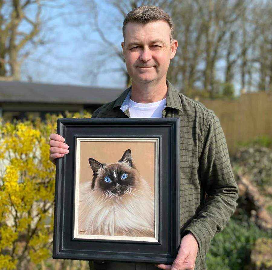 Nicholas Beall – traditional oil pet portrait artist showcasing his work Nicholas Beall, the artist, holding a finished oil portrait of a cat in his studio, demonstrating his work.