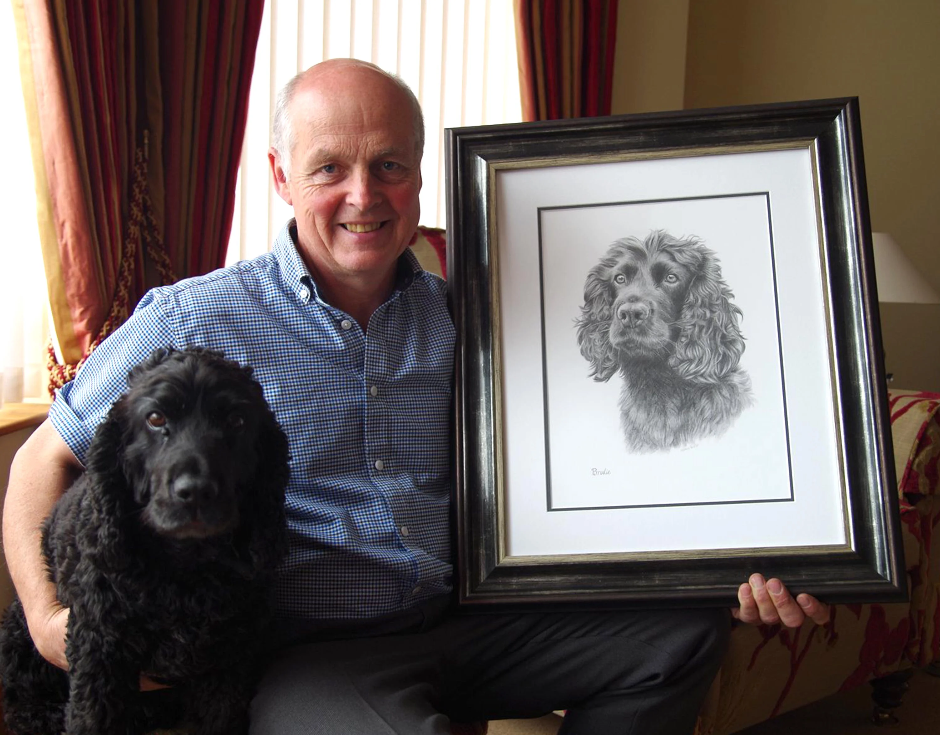 Classic pencil portrait of Brodie, a Cocker Spaniel, capturing his curled fur and expressive face, with graphite pencils placed on the left.