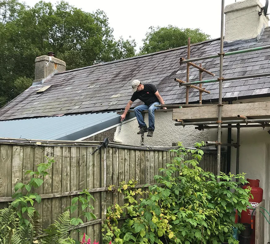 Nicholas Beall on scaffolding, actively engaged in painting the roof during cottage renovations in 2019.