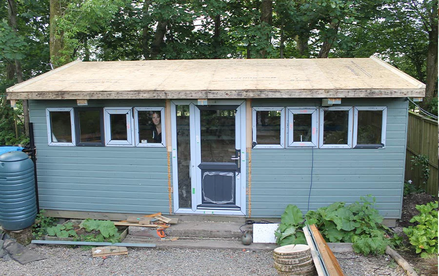 New Studio Roof, Door, and Windows Installed Exterior view of the renovated art studio, featuring the newly installed triple-layer felt roof, dark grey double-glazed door, and windows.