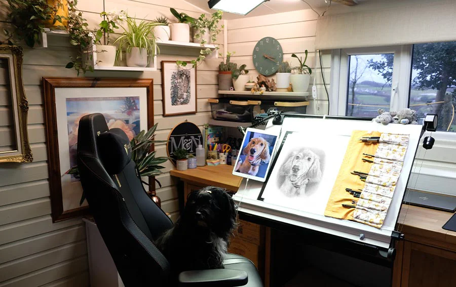 Melanie's Dedicated Studio Workspace for Pencil Drawings Melanie's organized drawing desk inside the art studio, featuring a tilted drawing board, laptop, and monitor setup for pencil portraits.