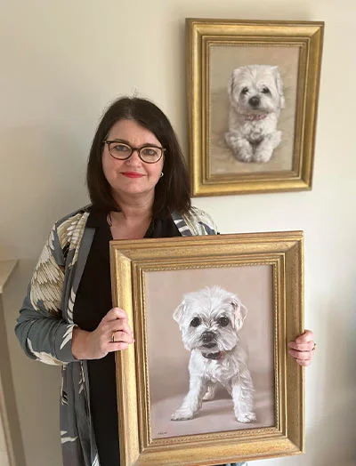 Client Sharon's Testimonial for Bobby and Paddy's Portraits Client Sharon holding her new pet portraits of Bobby and Paddy, showcasing Nicholas's talent in capturing their likeness.